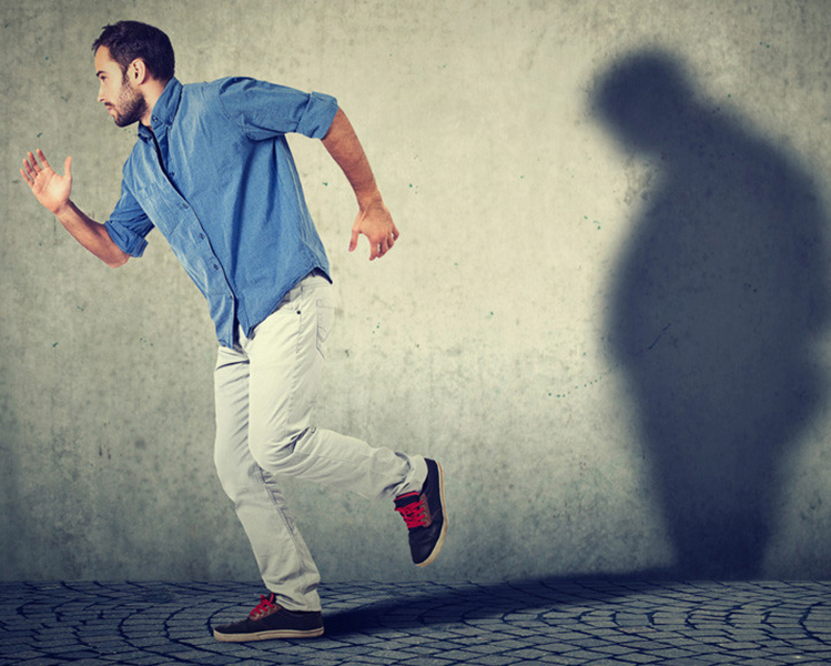 hombre corriendo con una sombra con sobrepeso en la pared