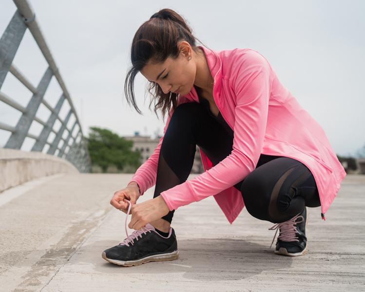 Mujer vestida de runner atando los cordones de su zapatilla